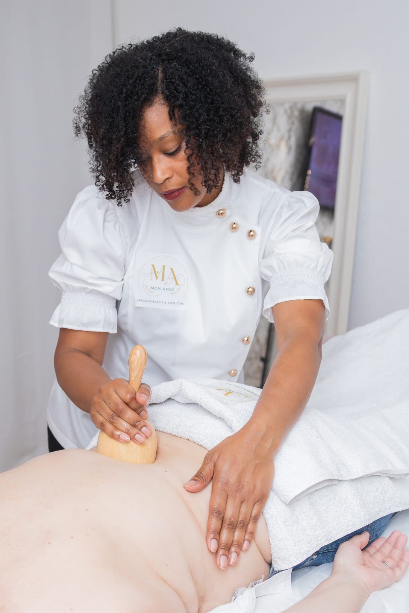 Massothérapeute utilisant un outil de madérothérapie en bois sur le dos d'une personne allongée.