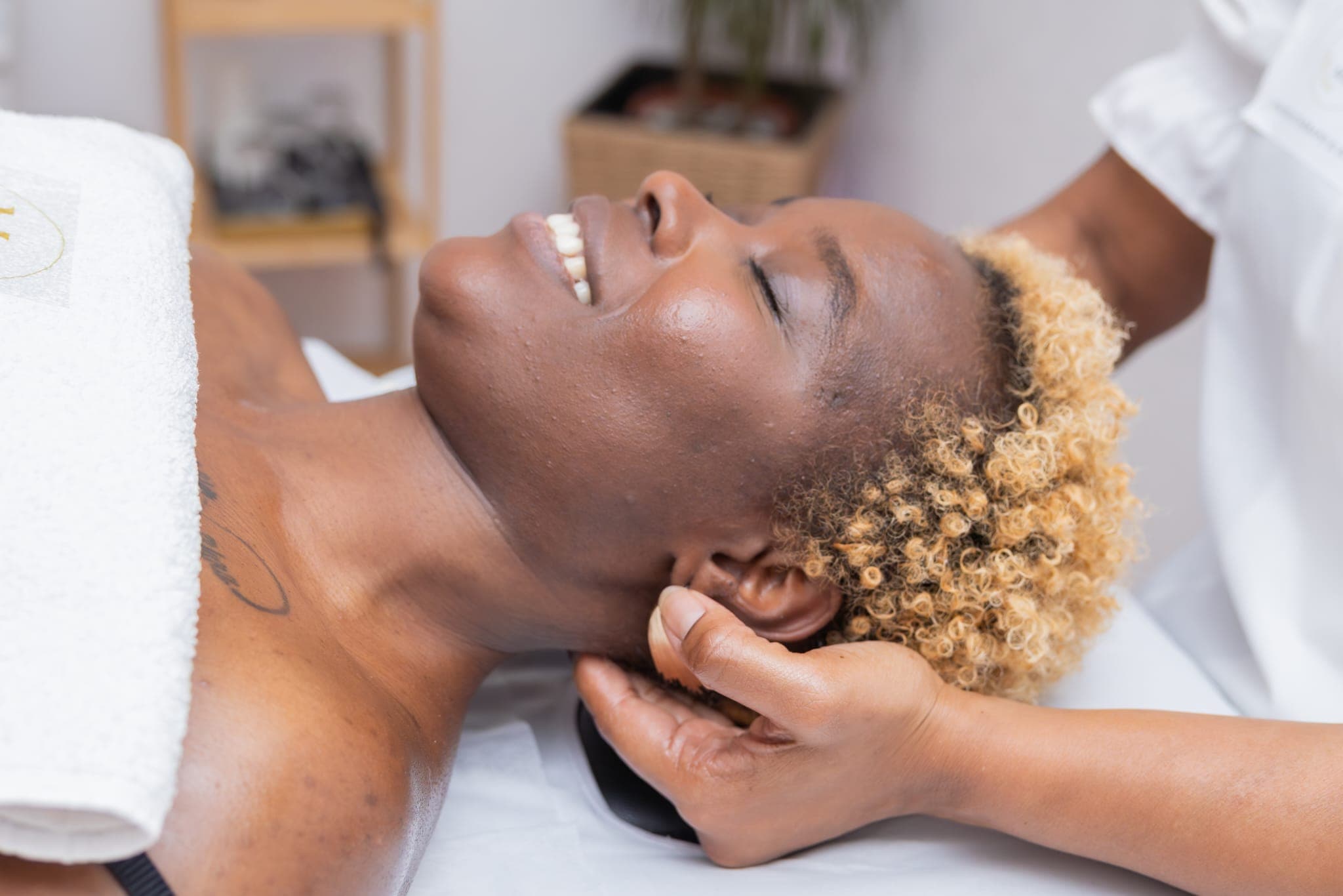 Femme noire souriante aux cheveux blonds bouclés recevant un massage de la tête relaxant.
