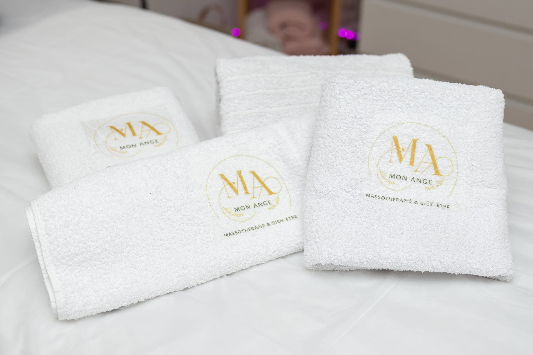 Serviettes blanches avec logo doré Mon Ange Massothérapie et Bien-être sur table de massage.